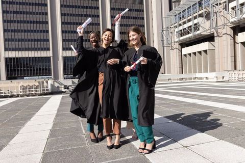 Triumphant diverse female graduates celebrating on urban rooftop holding diplomas