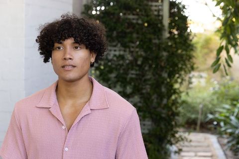 Young man in pink shirt relaxing in sunlit courtyard with vine-covered trellis