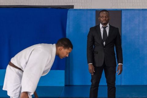 Coach in suit watches martial arts student on blue mats