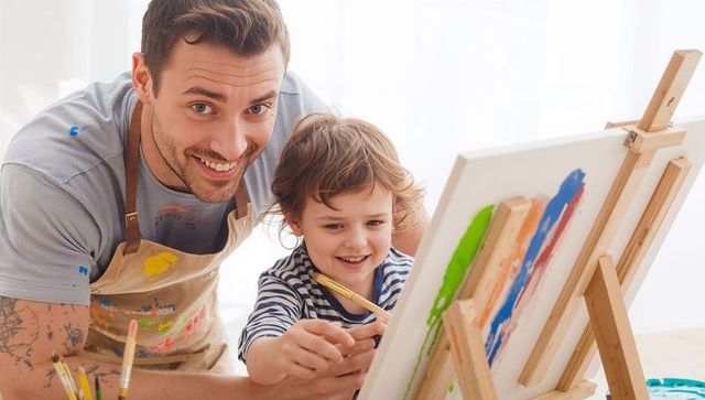 Father guiding young child painting on easel at home art corner, joyful creative bonding