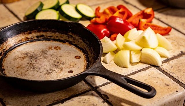 Cast iron skillet sitting among chopped zucchini, bell pepper and onion on tiled countertop
