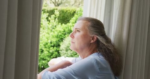 Senior Woman in Blue Shirt Contemplating Through Home Window