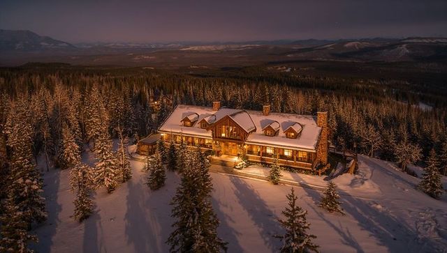 Glowing rustic mountain lodge nestled in snowy forest at twilight with warm porch light
