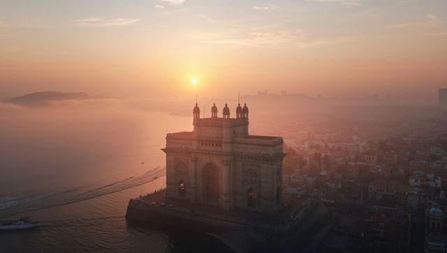 Gateway of india silhouetting at misty sunrise over mumbai harbor and waterfront skyline