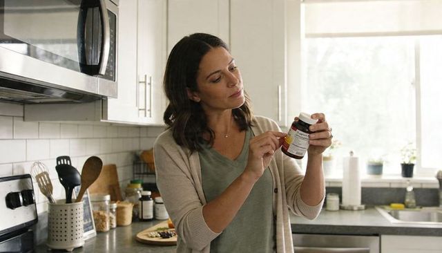 Woman reading supplement label in bright modern kitchen for wellness, nutrition, safe use