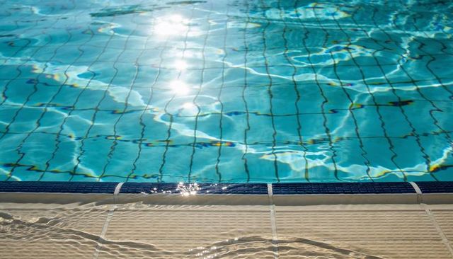 Sunlight shimmering on turquoise pool water along dark blue coping tiles