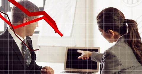 Business professionals pointing at laptop and analyzing falling red sales graph in meeting
