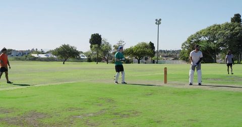 Batsman batting on suburban cricket pitch with wooden stumps, teammates on sunny park day