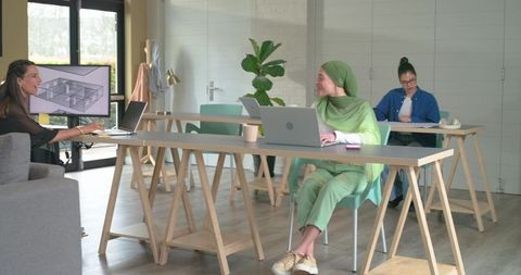 Diverse female team reviewing 3d architectural model on laptops in bright coworking office