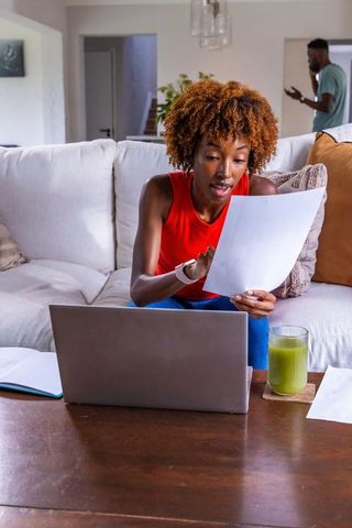 African american woman reviewing documents on laptop while on phone sipping green smoothie