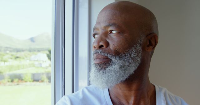 Side view of mature black man looking through window in a comfortable home. He is pensive and upset 4k