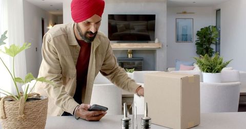 Man with Turban Scanning Package Barcode Using Smartphone in Modern Kitchen