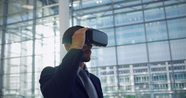 Businessman using virtual reality headset in a sleek, modern office building. Ideal for illustrating concepts of technology integration in business, corporate innovation, and the future of work in presentations, websites, and marketing materials related to tech advancements in the professional world.
