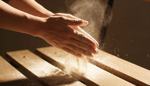 Hands clapping flour over wooden board creating cloud of baking dust and texture