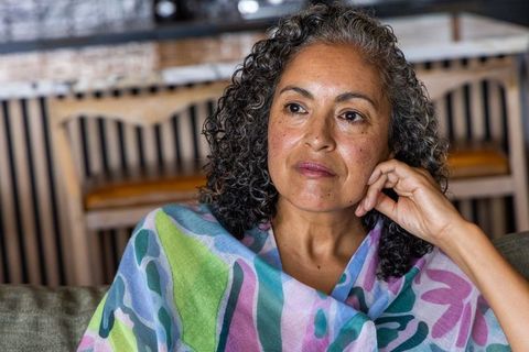 Contemplative african american woman sitting on sofa wearing colorful shawl