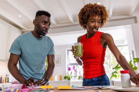 African american couple organizing home paperwork at kitchen counter with green smoothie