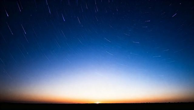 Long exposure star trails over rural horizon at dawn rising sun sliver and gradient sky