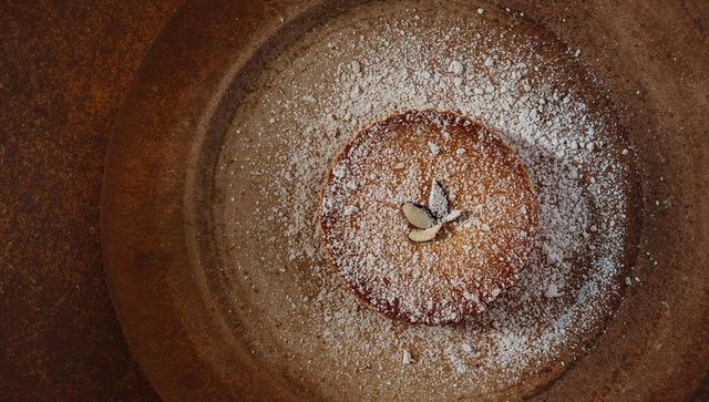 Almond tart sitting on rustic brown plate dusted with powdered sugar
