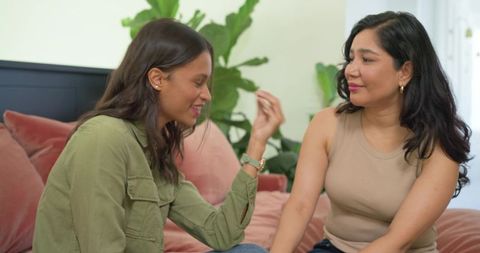 Diverse female friends sharing heartfelt conversation and laughter on cozy living room sofa