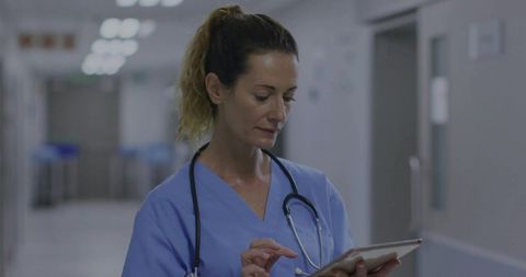 Dedicated doctor in scrubs reading tablet in hospital corridor
