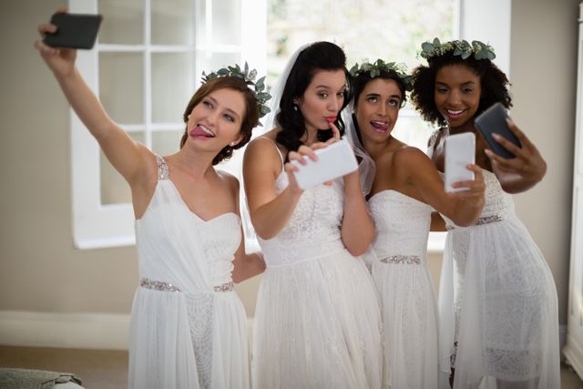Bride and bridesmaids taking a playful selfie indoors, capturing a joyful moment before the wedding ceremony. Ideal for use in wedding planning, bridal party inspiration, friendship celebrations, and social media content related to weddings and bridal parties.