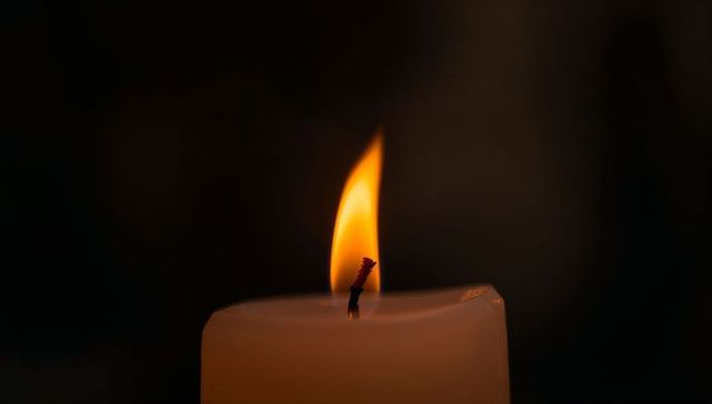 Ivory pillar candle burning with warm flame and melted wax against dark moody background