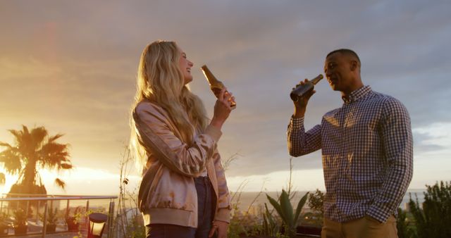 This image shows two friends enjoying beer while standing on a rooftop at sunset. It conveys a sense of relaxation and celebration in a picturesque outdoor setting. Ideal for use in promotional materials for leisure activities, beverage brands, travel advertisements, or social event posters.