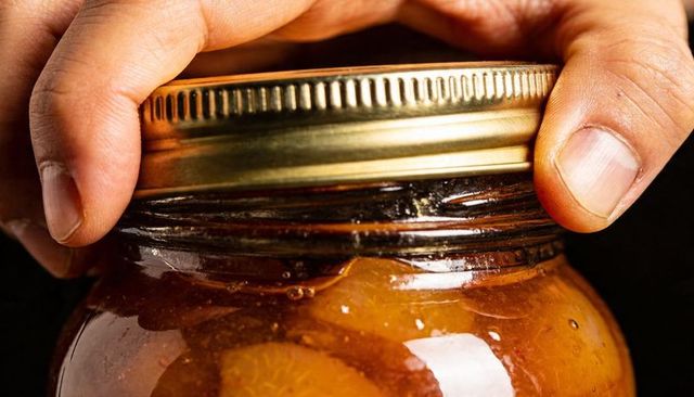 Twisting metal lid on jar of citrus marmalade close-up hands opening preserve