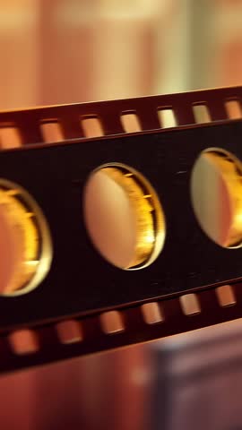 Sliding Filmstrip Moving Across Warm Studio with Shifting Golden Rings and Sprocket Hole Bokeh