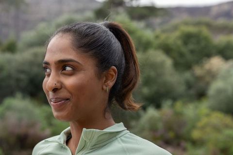 Indian woman standing on nature trail wearing light green zip-up top and smiling