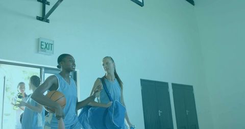 Female basketball players walking out gym carrying ball and duffel bags, showing camaraderie