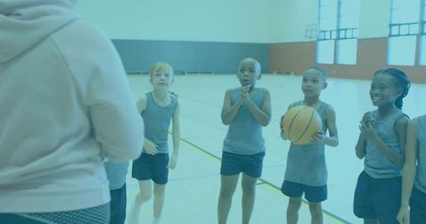 Youth basketball players listening to coach in gymnasium during practice and team drills