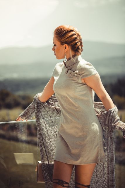 Woman with braided hair posing outdoors in elegant dress. Scenic background adds natural and sophisticated charm to the setting. Ideal for fashion editorial, lifestyle blogs, and outdoor fashion promotions.
