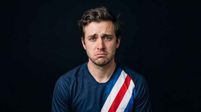 Man looking sad in studio headshot wearing navy shirt with red white blue diagonal stripe
