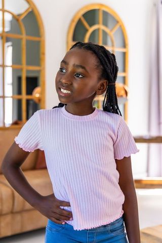 Confident african american girl posing hand on hip in casual pink top and jeans