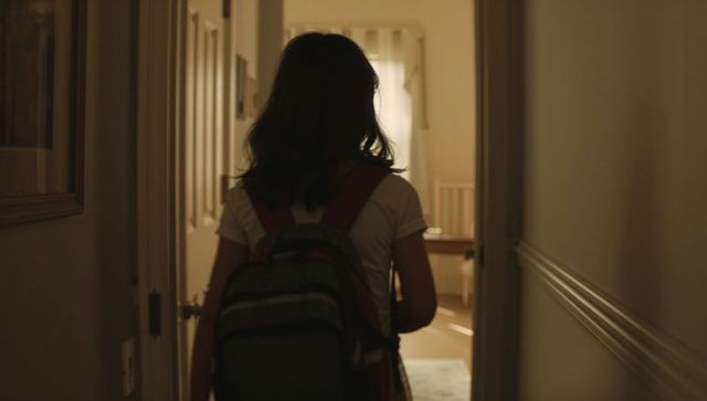 Teen girl walking down hallway toward nursery carrying backpack backlit silhouette