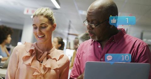 Colleagues collaborating over laptop showing social media notifications in open office