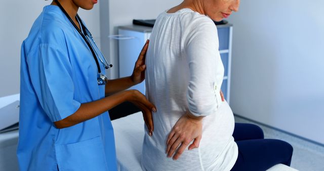 An African American nurse assists a pregnant Caucasian woman, with copy space. The nurse's supportive gesture and the woman's posture suggest a prenatal check-up or a discussion about pregnancy care.