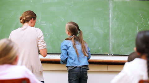 Student Writing on Classroom Blackboard with Teacher Assistance
