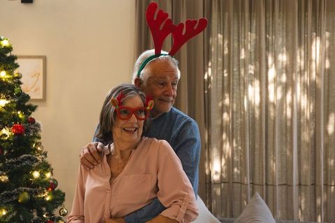 Senior couple embracing near christmas tree in festive antler headbands