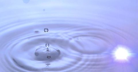 Serene water droplet creating concentric ripples with soft lens flare
