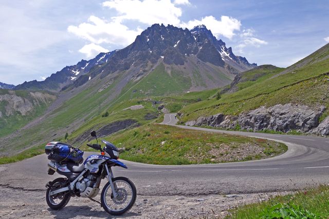 Motorcycle parked on winding mountain road against a backdrop of majestic peaks. Ideal for depicting freedom, adventure, and exploration. Perfect for travel advertisements, adventure blogs, tourism brochures, and scenic drive promotions.