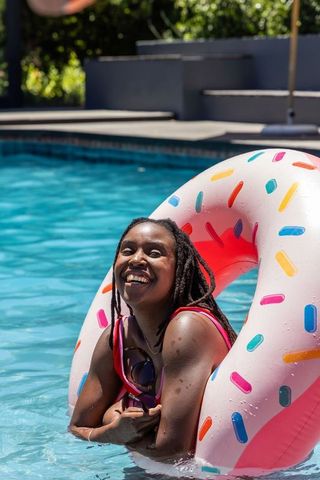 Smiling african american woman lounging on donut float with sprinkles in backyard pool