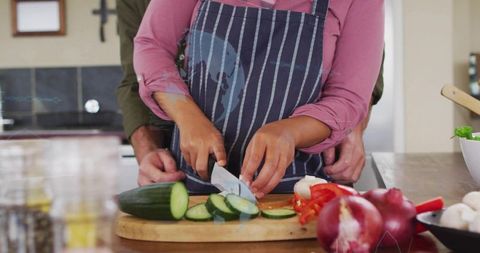 Couple cooking together slicing cucumber while partner guiding hands for safe knife skills