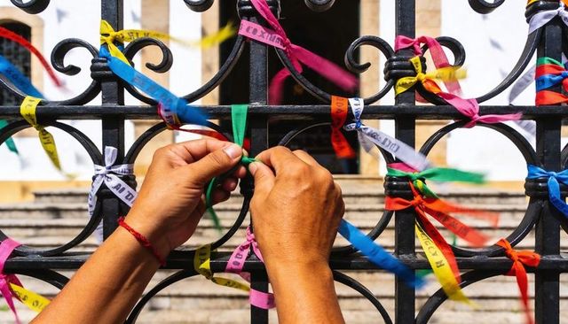 Hands tying green ribbon on wrought iron fence with colorful wishes and prayer ribbons