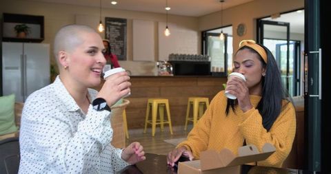 Multicultural friends sipping coffee at cozy cafe with takeout box and warm interior