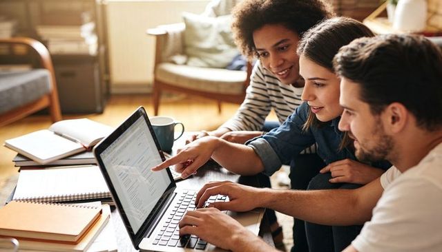Young adults collaborating on laptop in cozy living room studying, teamwork and planning
