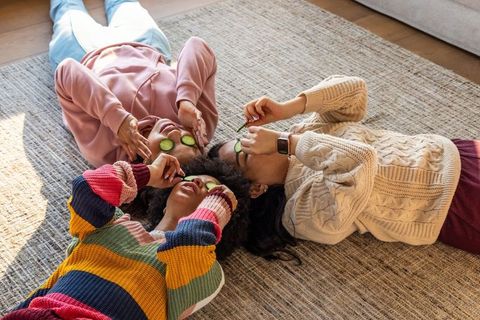 Friends enjoying at-home spa relaxing with cucumber eye slices on sunlit rug
