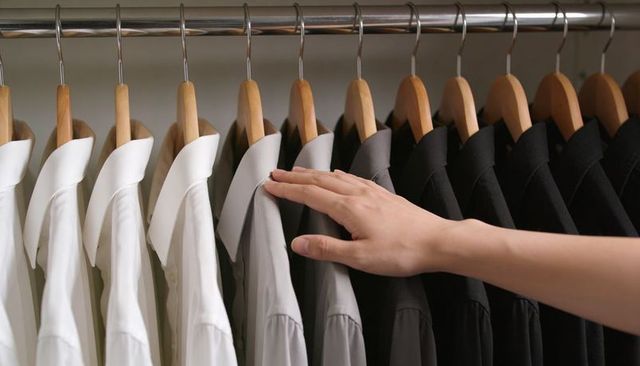 Hand selecting mid-gray button-down shirt from organized wardrobe white gray black shirts