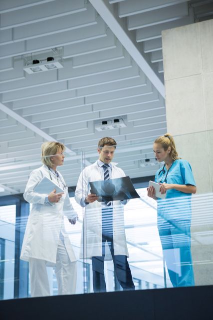 Medical team consisting of two doctors and a nurse discussing an x-ray report in a modern hospital corridor. Useful for illustrating medical teamwork, healthcare consultations, and professional medical environments. Ideal for healthcare websites, medical articles, and hospital brochures.